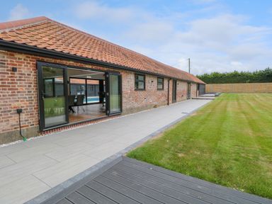 A brick building with a tiled roof and large glass doors opening to a tiled patio and a lawn at County Farm Barn in South Walsham
