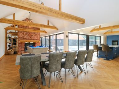 A dining area with a long table and chairs next to a pool table and a kitchen with bar stools at County Farm Barn in South Walsham