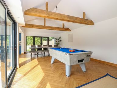 A room with a pool table and a dining table with chairs under wooden beams at County Farm Barn in South Walsham