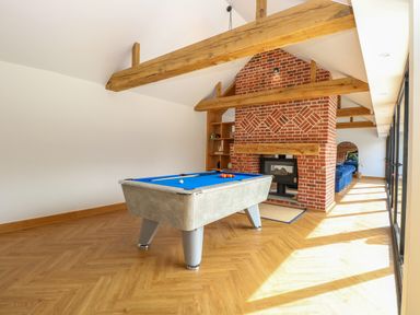 A room with a pool table a brick fireplace wooden beams and large windows at County Farm Barn South Walsham
