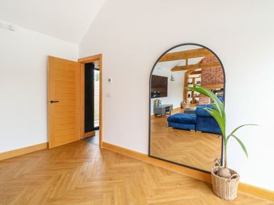 A wooden floor hallway with an open wooden door a large arched mirror reflecting a living room and a plant in a woven basket at County Farm Barn in South Walsham