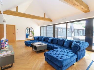A living room with a blue sectional sofa a coffee table wooden beams and sliding glass doors at County Farm Barn in South Walsham