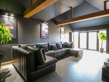 A living room with a black leather sectional sofa posters on the wall and plants near windows at County Farm Barn in South Walsham