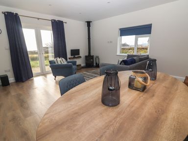 A living room with blue armchairs, a grey sofa, a wood stove, and a wooden table with candle holders at The Boathouse in Carrigaholt County Clare
