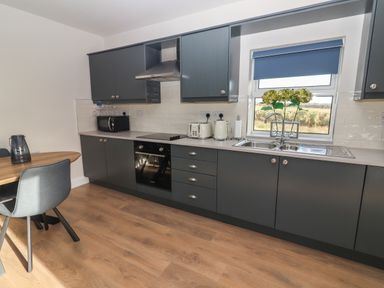 A kitchen with gray cabinets a sink toaster microwave and dining table at The Boathouse in Carrigaholt County Clare