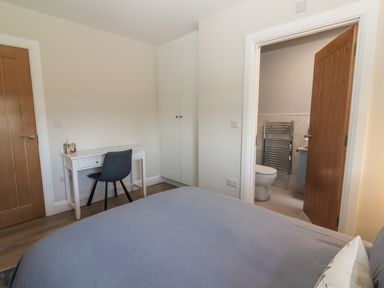 A bedroom with a bed a white desk and chair built in wardrobes and an open door to a bathroom at The Boathouse in Carrigaholt County Clare