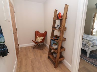 A small corner with a wooden ladder shelf and a leather chair with a pillow at The Boathouse in Carrigaholt County Clare
