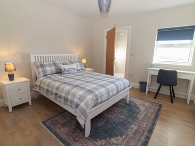 A bedroom with a bed a rug two bedside tables with lamps a desk and chair and a door leading to a bathroom at The Boathouse in Carrigaholt County Clare