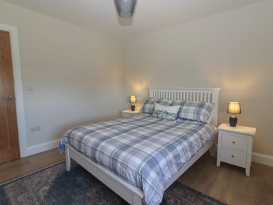 A bedroom with a bed with plaid bedding two bedside tables with lamps and a wooden door at The Boathouse in Carrigaholt County Clare