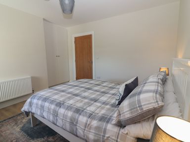 A bedroom with a bed with plaid bedding a wooden door a white wardrobe and a radiator at The Boathouse in Carrigaholt County Clare
