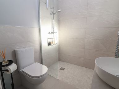 A bathroom with a toilet shower area and sink with beige tiles at The Boathouse in Carrigaholt County Clare