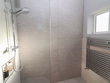 A shower area with a handheld showerhead a niche with toiletries a window and a wall-mounted towel radiator at The Boathouse in Carrigaholt County Clare