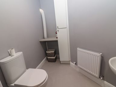 A bathroom with a toilet a radiator a small white cabinet and a wicker basket at The Boathouse in Carrigaholt County Clare