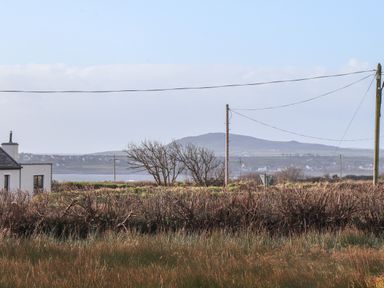 A rural landscape with grass, a small white house, utility poles, and hills in the background at The Boathouse in Carrigaholt County Clare