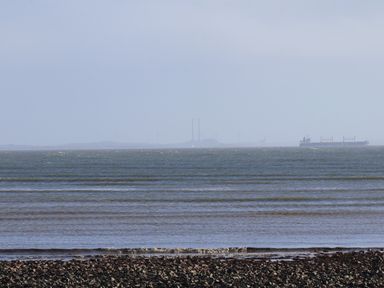 A rocky shoreline with waves and a cargo ship visible in the distance at The Boathouse in Carrigaholt County Clare