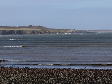 A rocky shoreline with waves and a grassy cliff in the distance at The Boathouse in Carrigaholt County Clare