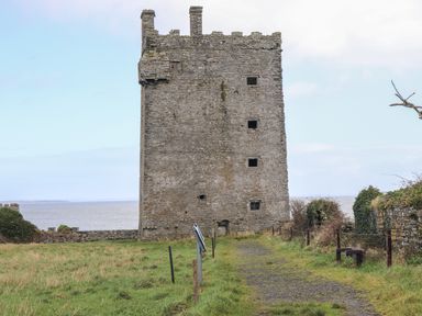 A stone tower with small windows near a grassy path and a body of water at The Boathouse in Carrigaholt County Clare