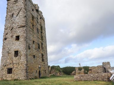An old stone tower and ruins on grass under a cloudy sky