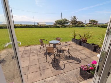 A patio with chairs and a table overlooking a grassy area at The Boathouse in Carrigaholt, County Clare