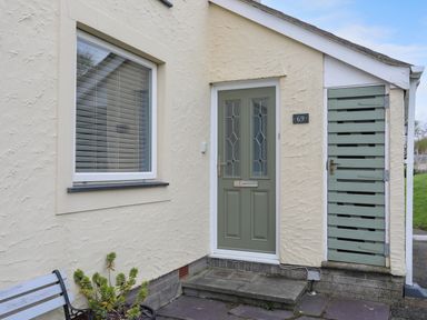 The exterior front entrance of a house with a green door a window a wooden bench and a small gate at Waters Edge Ymyl Y Dwr in Y Felinheli