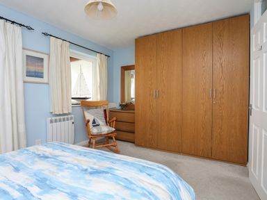 A bedroom with wooden wardrobes a wooden chair with cushions a dresser with a mirror and blue walls at Waters Edge Ymyl Y Dwr in Y Felinheli
