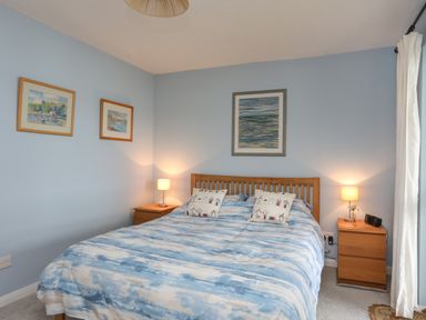 A bedroom with a wooden bed frame two bedside tables with lamps and framed pictures on the walls at Waters Edge Ymyl Y Dwr in Y Felinheli