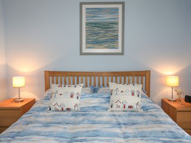 A bedroom with a wooden bed frame bedside tables lamps and a framed artwork above the bed at Waters Edge Ymyl Y Dwr in Y Felinheli
