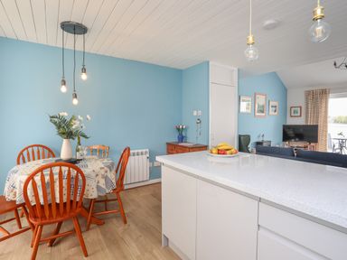 A dining area with a table and four chairs next to a kitchen island and a living room with a television at Waters Edge Ymyl Y Dwr in Y Felinheli