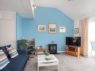 A living room with a blue wall sofa armchair coffee table and television at Waters Edge Ymyl Y Dwr in Y Felinheli