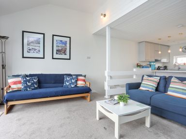 A living room with blue sofas and a white coffee table with plants and magazines at Waters Edge Ymyl Y Dwr in Y Felinheli