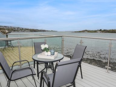 A balcony with a round table and four chairs overlooking a body of water at Waters Edge Ymyl Y Dwr in Y Felinheli