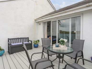 A patio with a round glass table and four chairs and a bench with cushions at Waters Edge Ymyl Y Dwr in Y Felinheli