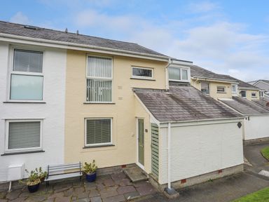 Exterior view of a row of attached houses with windows and doors with potted plants and a bench outside at Waters Edge Ymyl Y Dwr in Y Felinheli