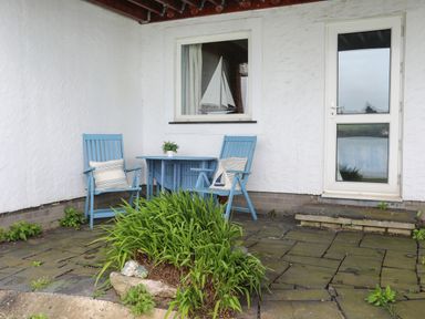 An outdoor patio area with two blue chairs a blue table a plant on the table and green plants in front at Waters Edge Ymyl Y Dwr in Y Felinheli