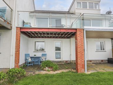 A patio area with blue chairs and table under a balcony with glass railing at Waters Edge Ymyl Y Dwr in Y Felinheli