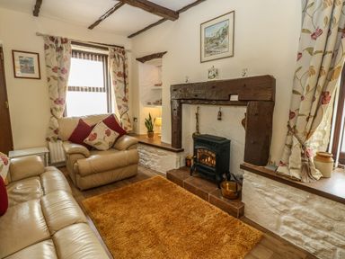 A living room with beige leather sofas a fireplace with wooden mantel and floral curtains at River Cottage in Eamont Bridge