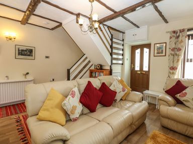 A living room with beige leather sofas with red and yellow cushions wooden floor and ceiling beams at River Cottage in Eamont Bridge