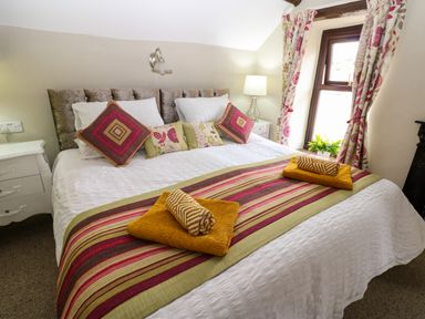 A bedroom with a bed with pillows and folded towels on a runner next to a window with floral curtains at River Cottage in Eamont Bridge