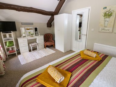A bedroom with a bed with folded towels a vanity table an armchair a wardrobe and a wall-mounted mirror at River Cottage in Eamont Bridge