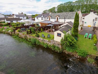 A row of houses with gardens next to a river at River Cottage in Eamont Bridge