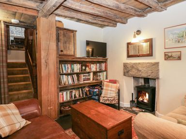 A living room with wooden ceiling beams a bookshelf a fireplace and a wooden chest at Eden Vale in Broughton-In-Furness