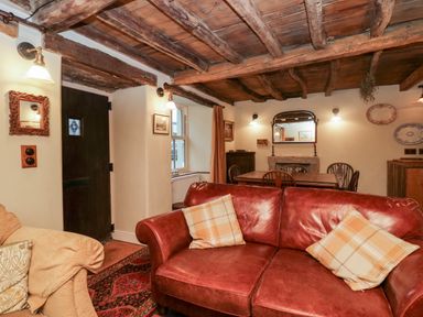 A living room with a red sofa, a wooden dining table, chairs, a mirror above a fireplace, and wooden ceiling beams at Eden Vale in Broughton-In-Furness