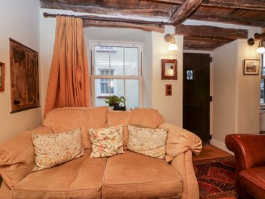 A living room with a beige sofa and patterned cushions next to a window with curtains at Eden Vale in Broughton-In-Furness