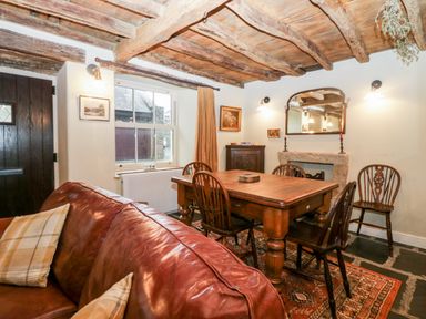 A dining room with wooden table and chairs a leather sofa and exposed wooden beams on the ceiling at Eden Vale in Broughton-In-Furness