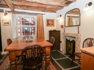A dining room with a wooden table and chairs a window with curtains a fireplace with a mirror and candles at Eden Vale in Broughton-In-Furness