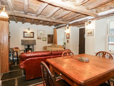 A living room with a wooden dining table and chairs a leather sofa and a fireplace with exposed wooden beams on the ceiling at Eden Vale Broughton-In-Furness