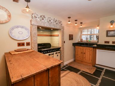 A kitchen with wooden cabinets and island a stove set in a stone alcove and plates on the wall at Eden Vale in Broughton-In-Furness