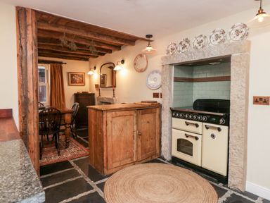 A kitchen with a wooden island a black and cream stove a dining table with chairs and wooden ceiling beams at Eden Vale in Broughton-In-Furness