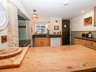A kitchen with wooden countertops wooden cabinets a stone fireplace and a window at Eden Vale in Broughton-In-Furness