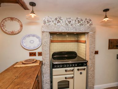 A kitchen stove in a stone alcove with decorative plates mounted on the wall and wooden countertop with cutting boards at Eden Vale in Broughton In Furness